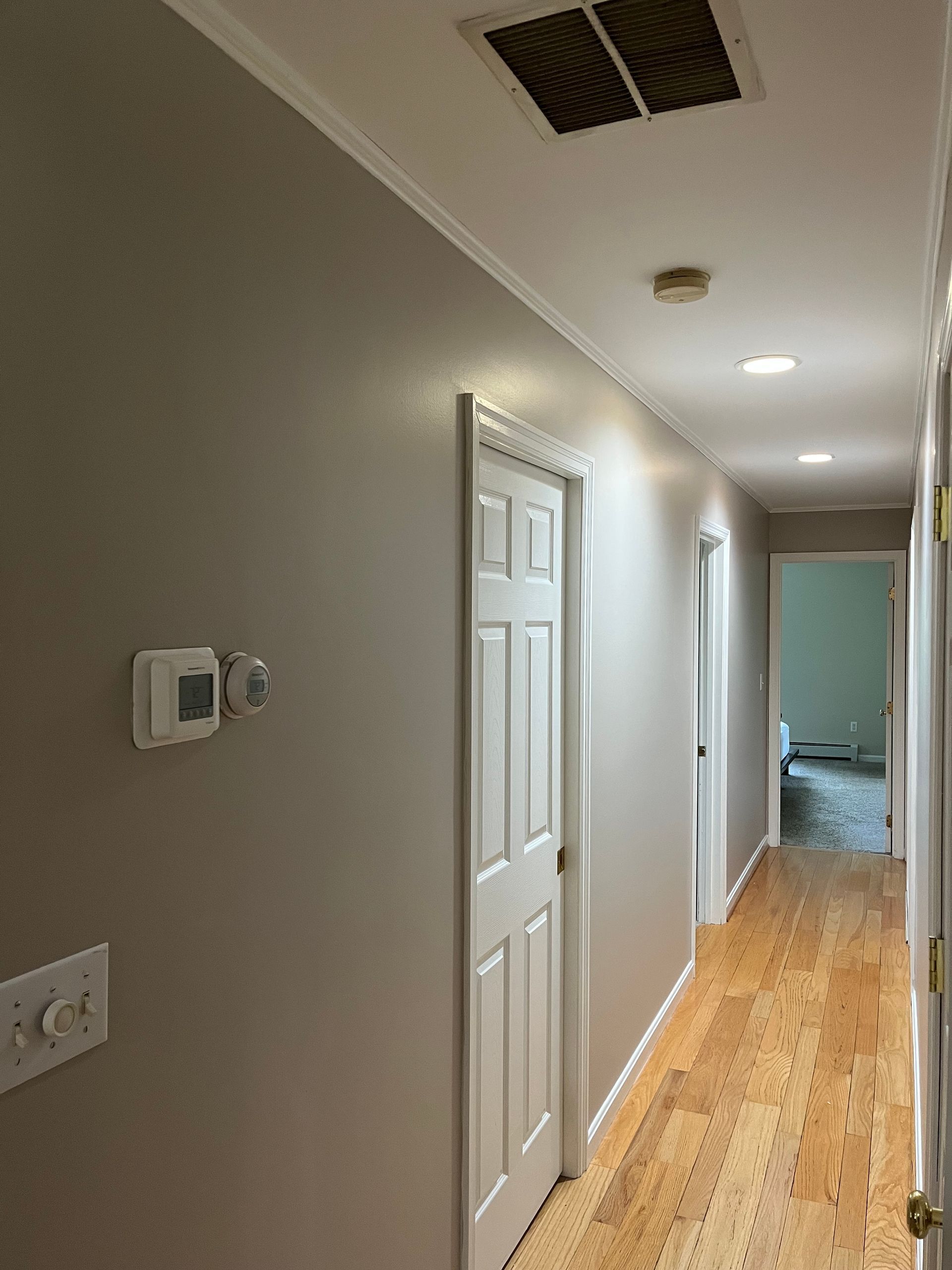 Hallway with wood floor, white doors, tan walls, and recessed lighting. Thermostat on the wall.