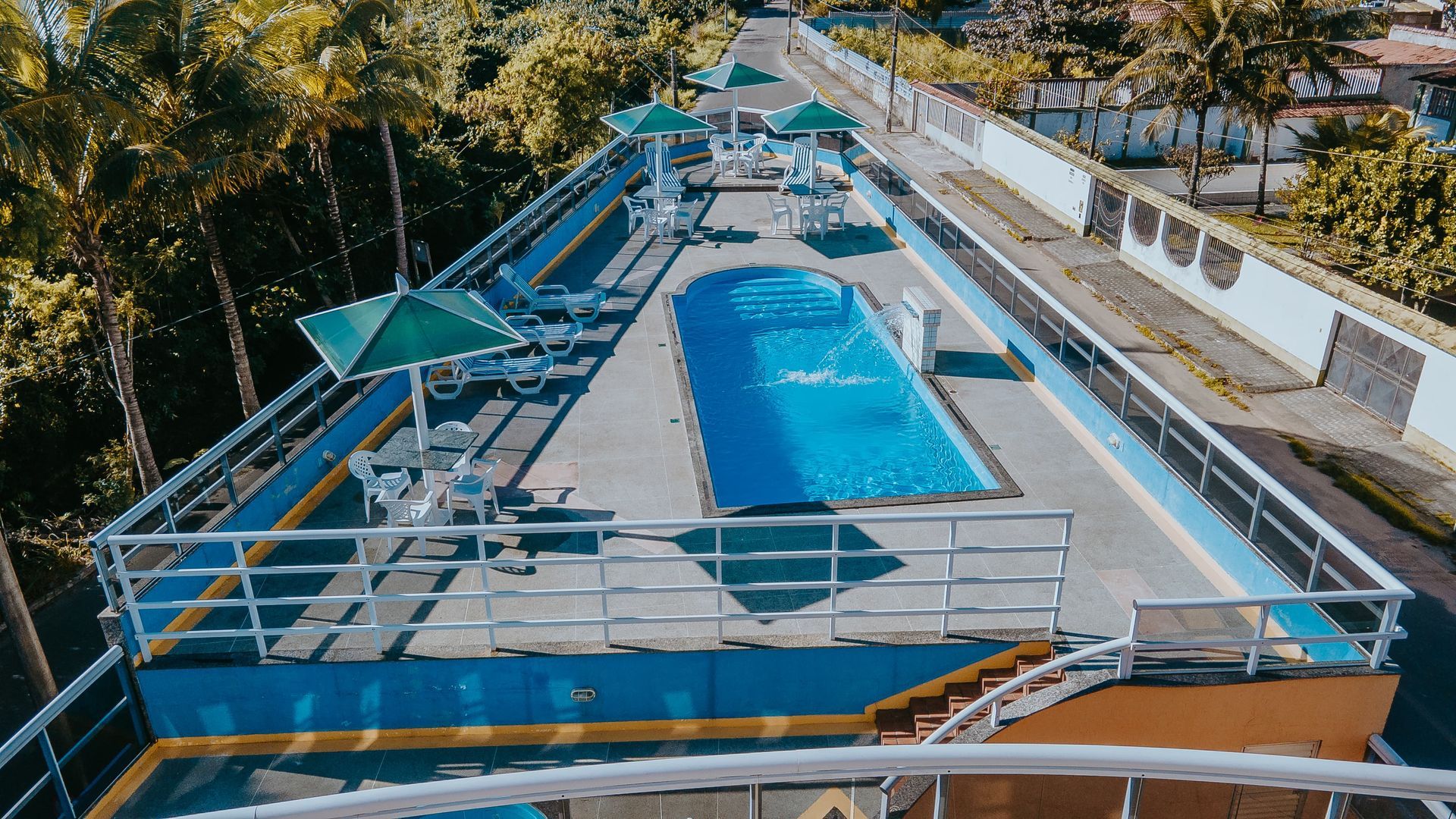 Piscina na cobertura com água azul, cercada por grades e com árvores ao fundo.