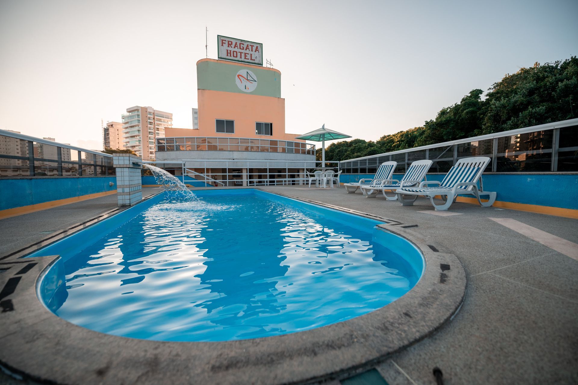 Piscina ao ar livre na cobertura com água azul e espreguiçadeiras ao pôr do sol.