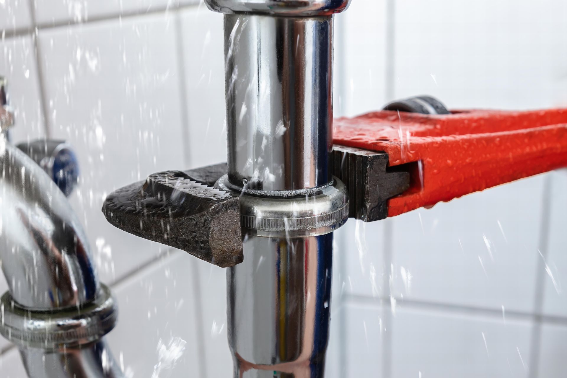A plumber is fixing a leak in a bathroom with a wrench.