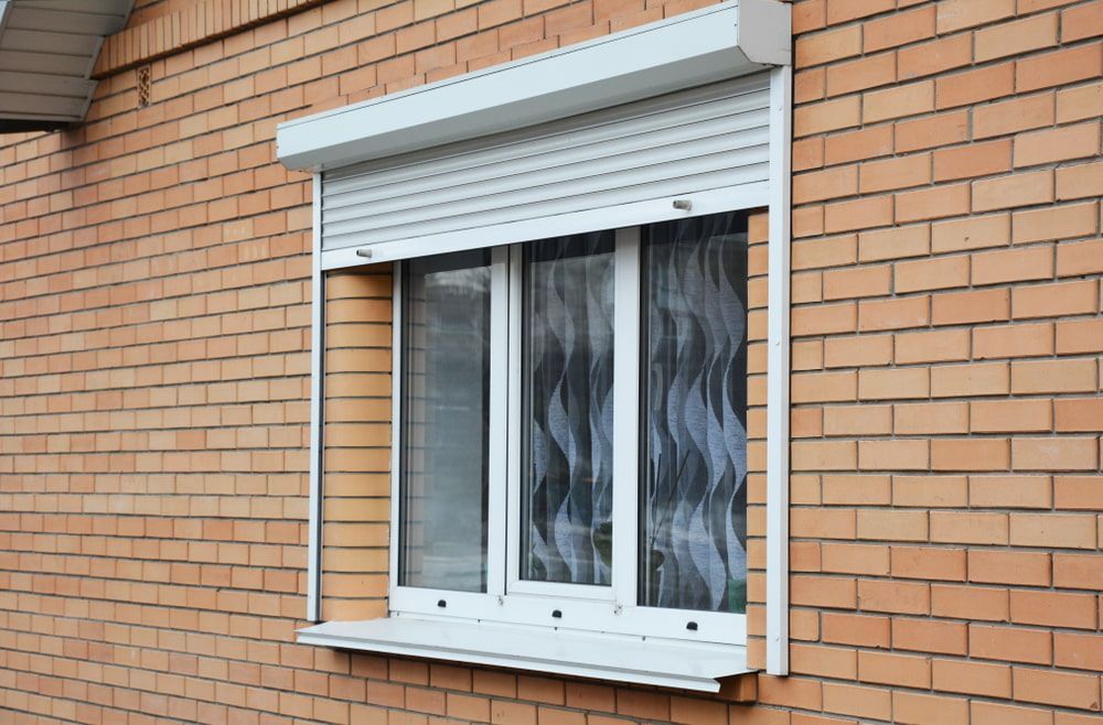 Window with closed white security shutter, brick building exterior.
