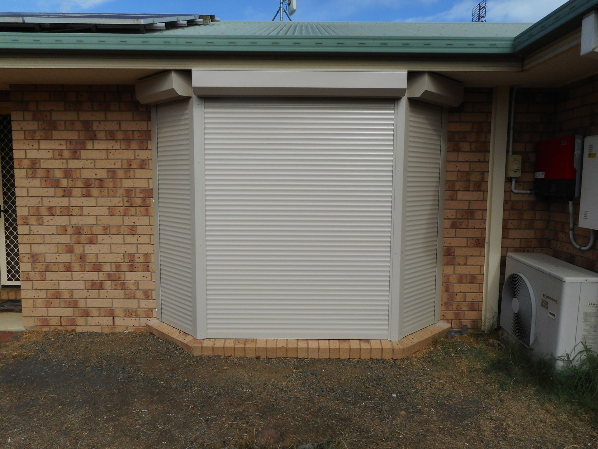 a Brick Building With a Closed Gray Security Roller Shutter — Toowoomba Shade & Canvas in Harristown, QLD