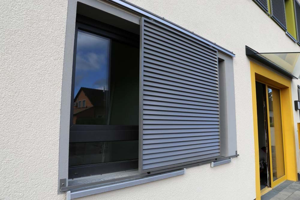 Gray Sliding Shutter Partially Covering a Window on a Beige Building — Toowoomba Shade & Canvas in Harristown, QLD