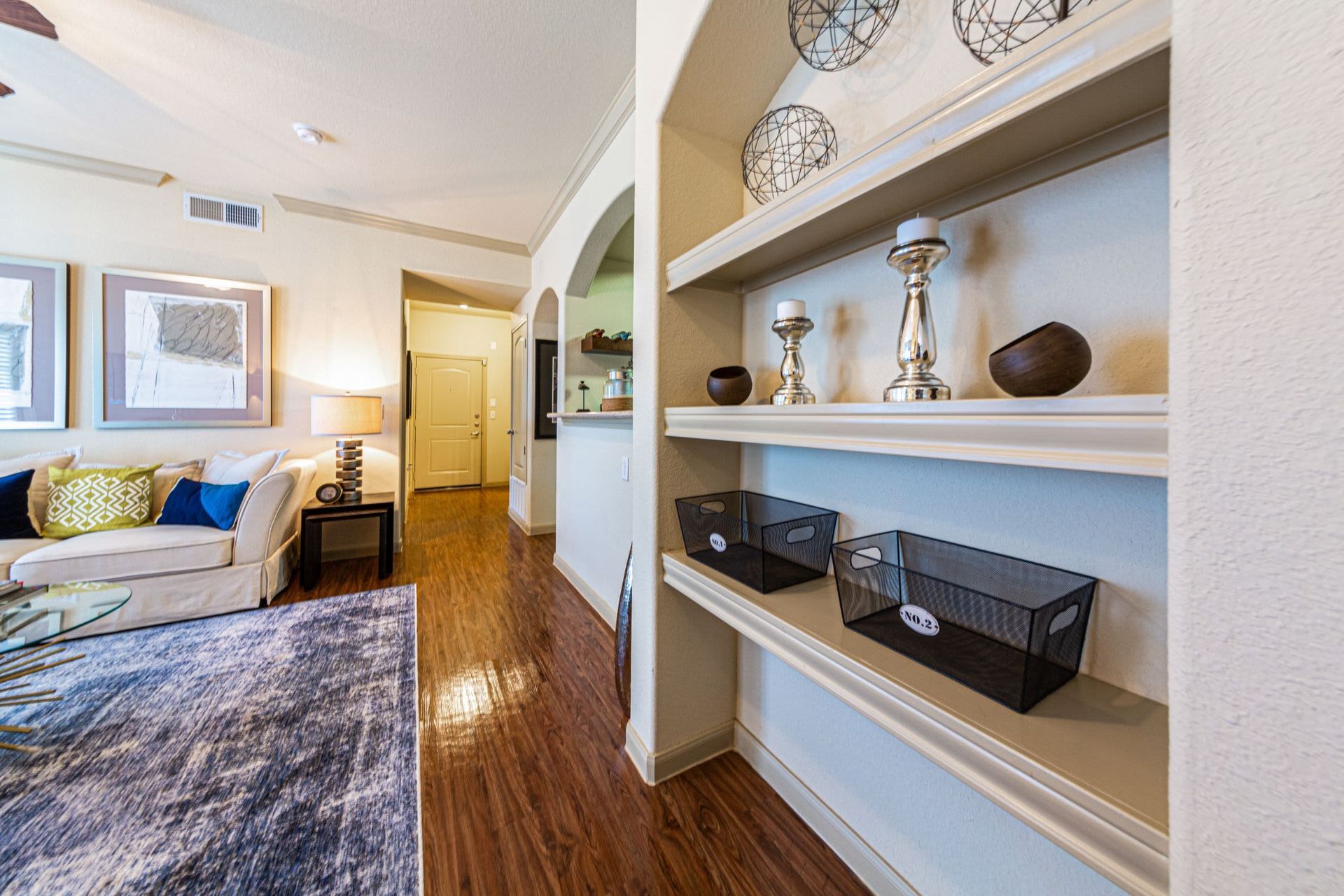 A living room with hardwood floors, a couch, and shelves at Marquis Grand Lakes in Richmond, TX.