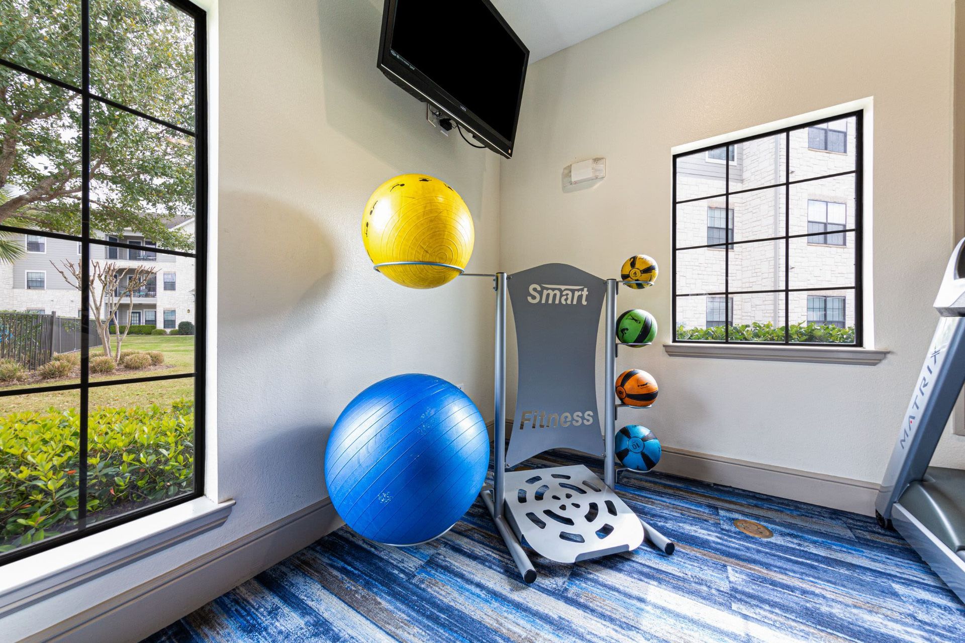 A gym with a treadmill, exercise balls, and a television at Marquis Grand Lakes in Richmond, TX.