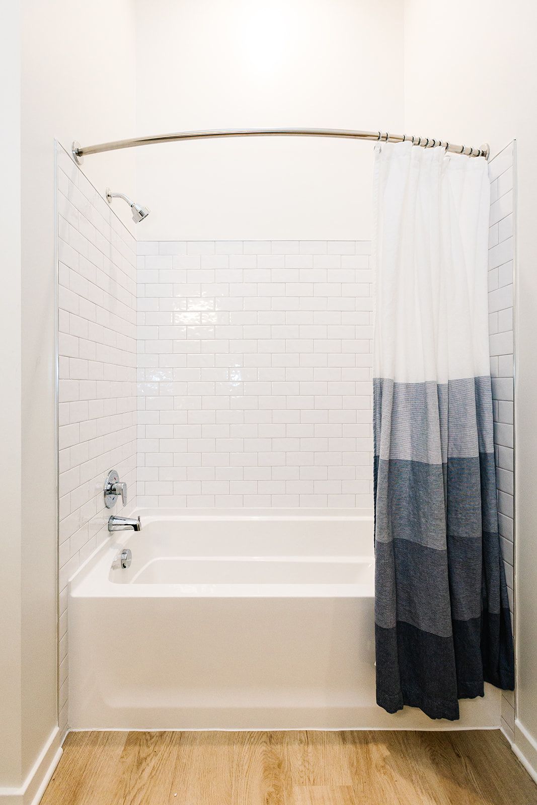 White bathroom with a tub, subway tile wall, and a blue-gray shower curtain at Opal Largo Station Apartments in Largo, MD