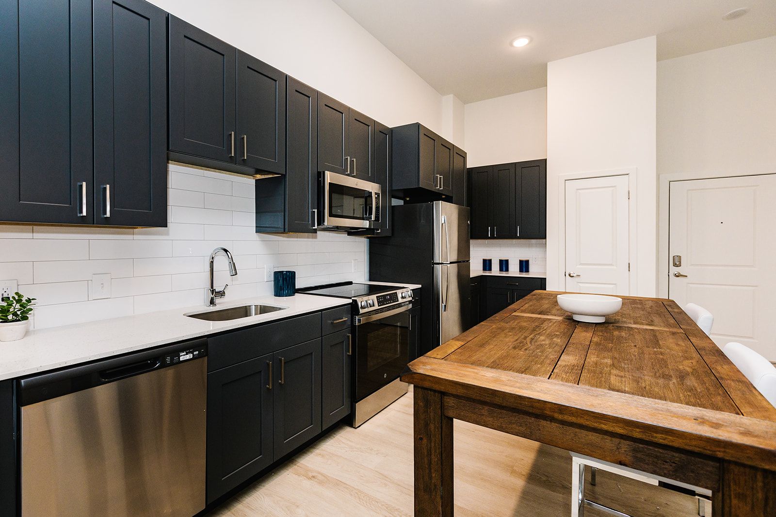 Modern kitchen with black cabinets, white countertops, and a rustic wooden island table at Opal Largo Station Apartments in Largo, MD