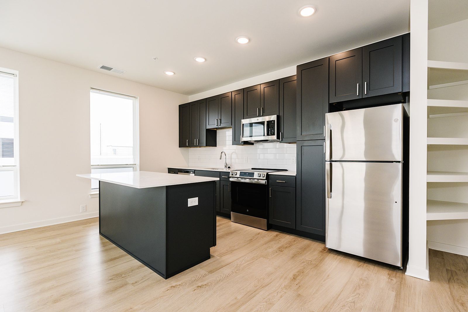Modern kitchen with black cabinets, stainless steel appliances, island, and light wood floors at Opal Largo Station Apartments in Largo, MD