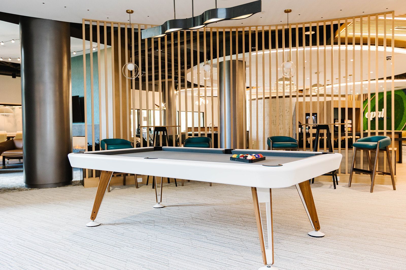 Modern lounge with white pool table, wood slat dividers, and blue chairs in a bright open space at Opal Largo Station Apartments in Largo, MD