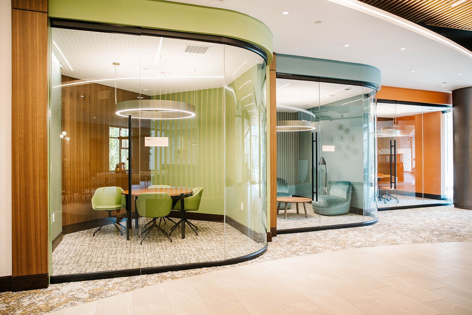 Modern office lounge pods with glass walls, curved booths, and green chairs in a bright hallway at Opal Largo Station Apartments in Largo, MD