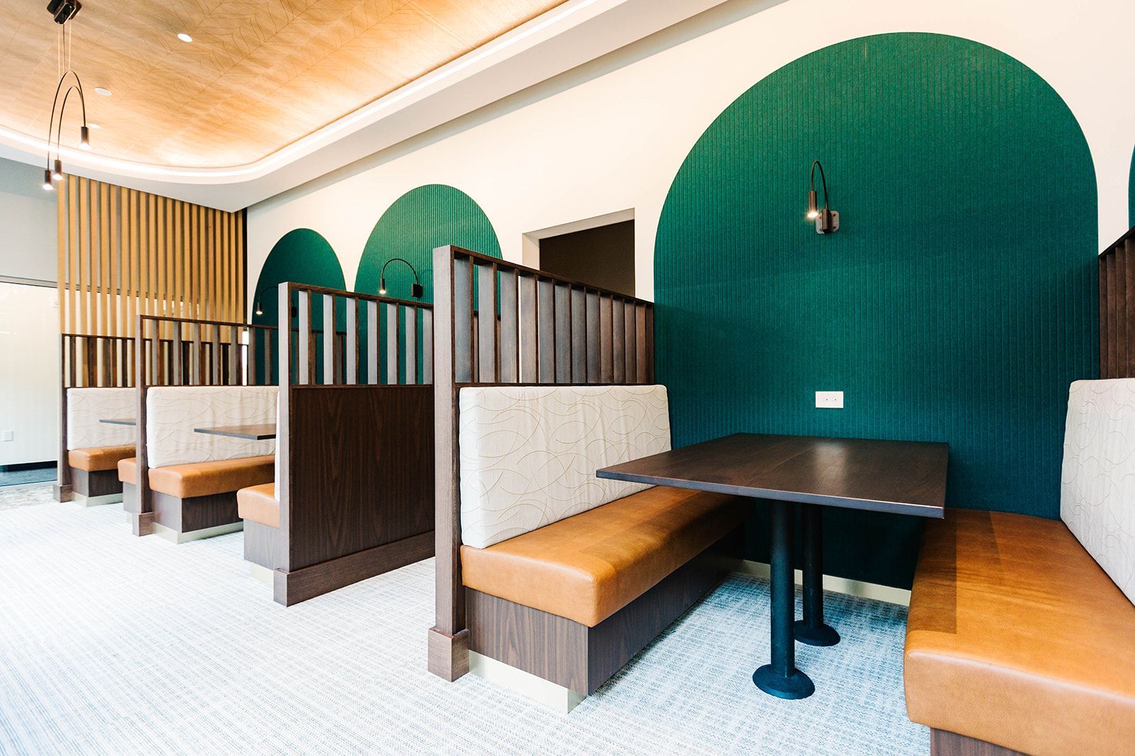 Modern café booths with dark wood partitions, tan benches, and large green arch wall accents at Opal Largo Station Apartments in Largo, MD