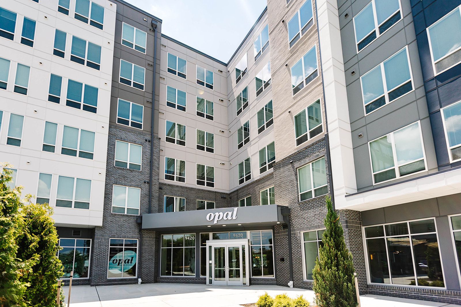 Modern apartment building courtyard with glass entrance and landscaped greenery at Opal Largo Station Apartments in Largo, MD