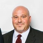 A bald man in a suit and tie is smiling for the camera.