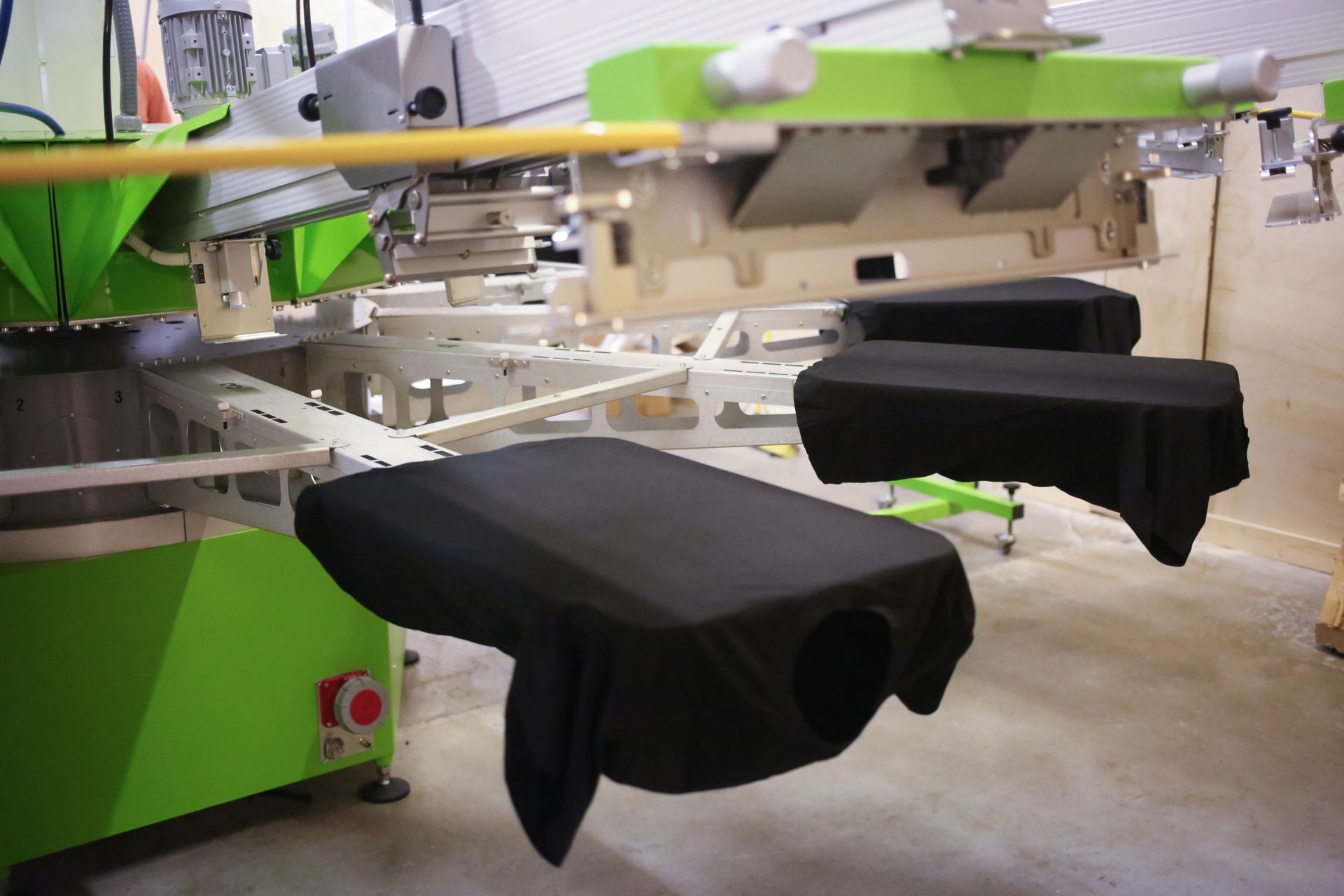 Screen printing machine with black shirts loaded on pallets, ready to print. Green and gray machine.