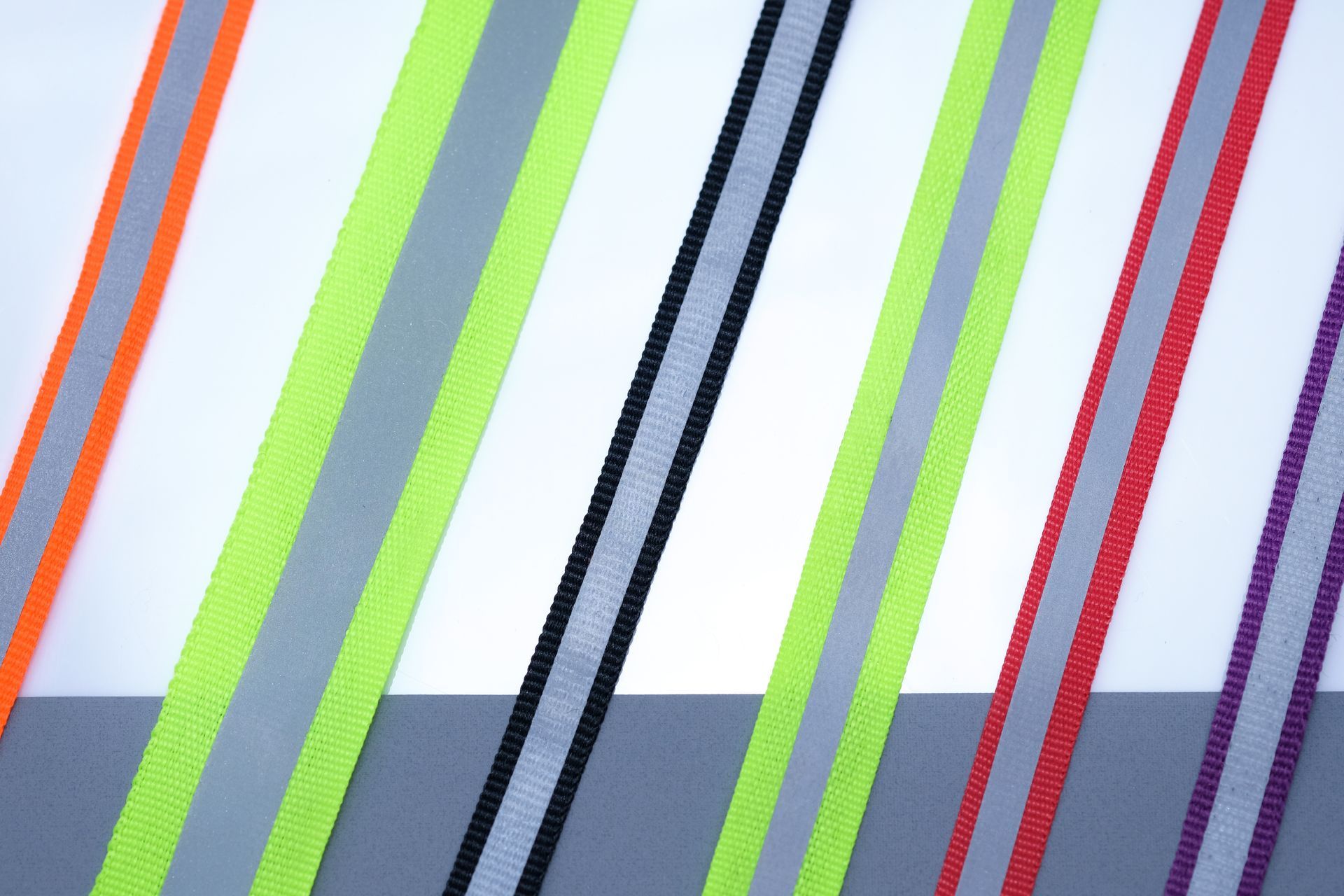 Various diagonal reflective safety strips: orange, green, black, gray, red, and purple on a white and gray surface.