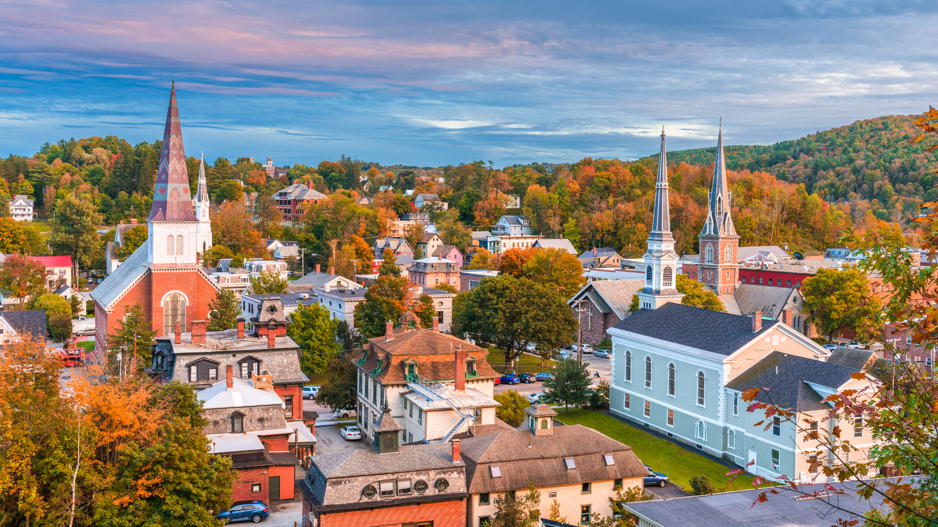 Colorful hillside town with church steeples, white buildings, and autumn trees under a blue sky
