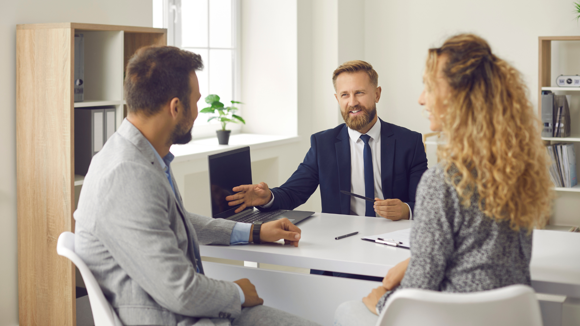 Business meeting in a bright office, with three people discussing documents around a table.