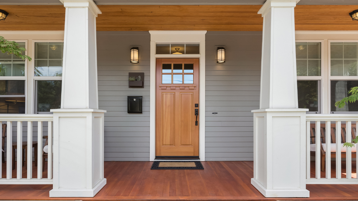 Front porch with a wooden front door, white columns, and gray siding on a house