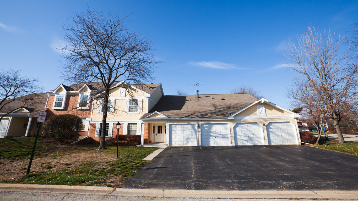 Suburban house with three-car garage and bare trees along a paved driveway