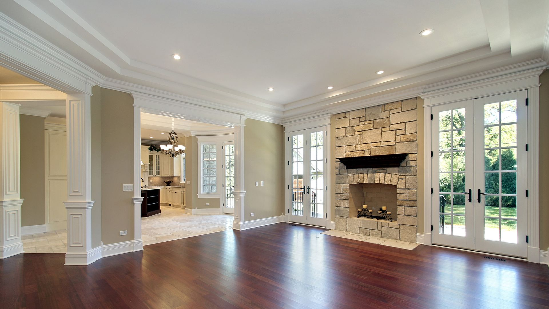 Empty living room with wood floors, stone fireplace, French doors, and light-colored walls.
