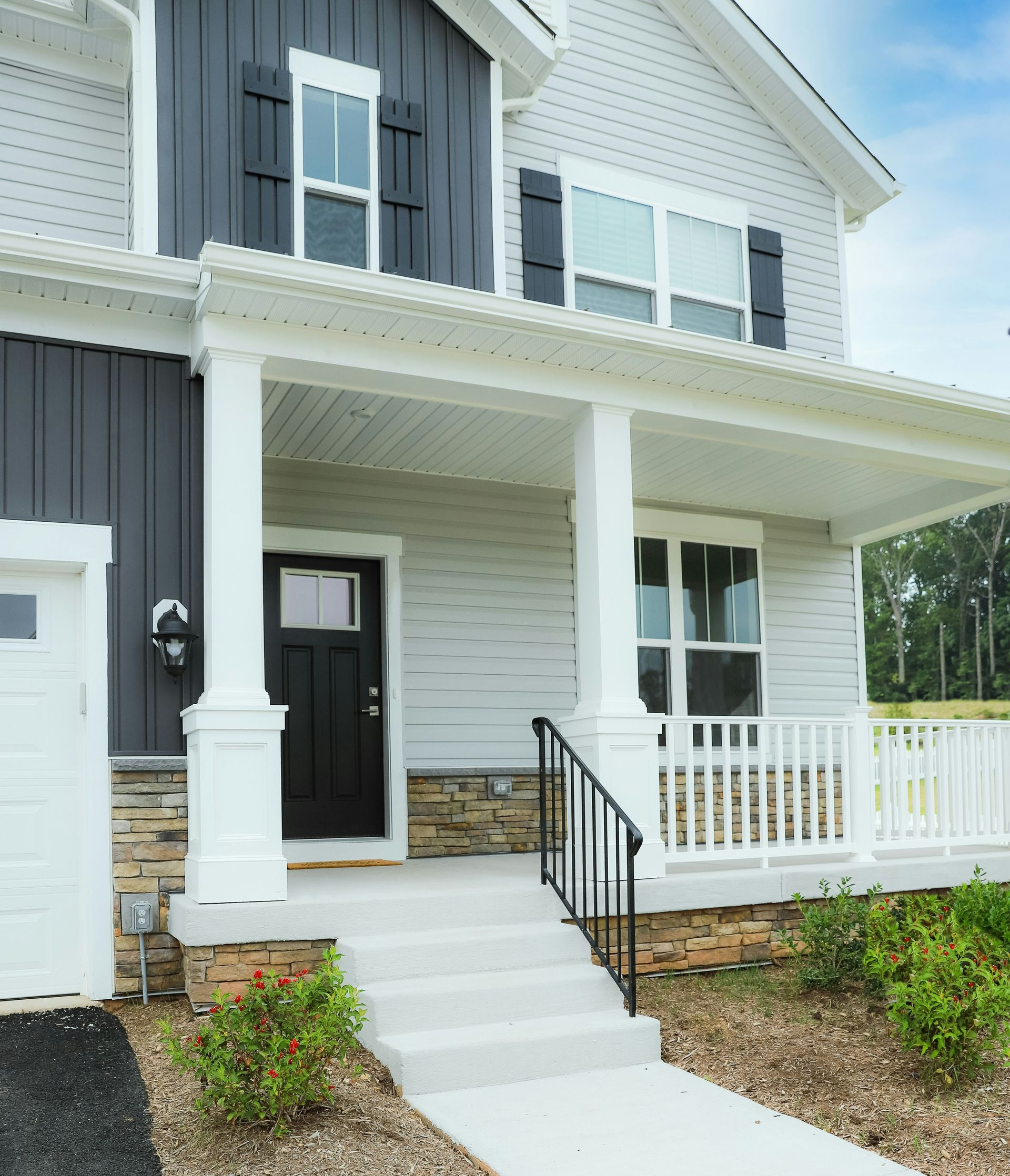 Front porch of a gray and white house with steps, railing, and a black front door.