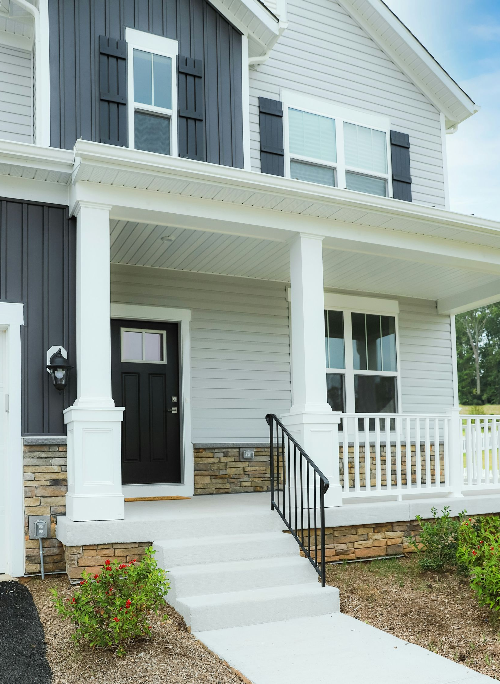 A two-story house exterior with light grey siding, dark board-and-batten accents, a stone foundation, and a front porch.