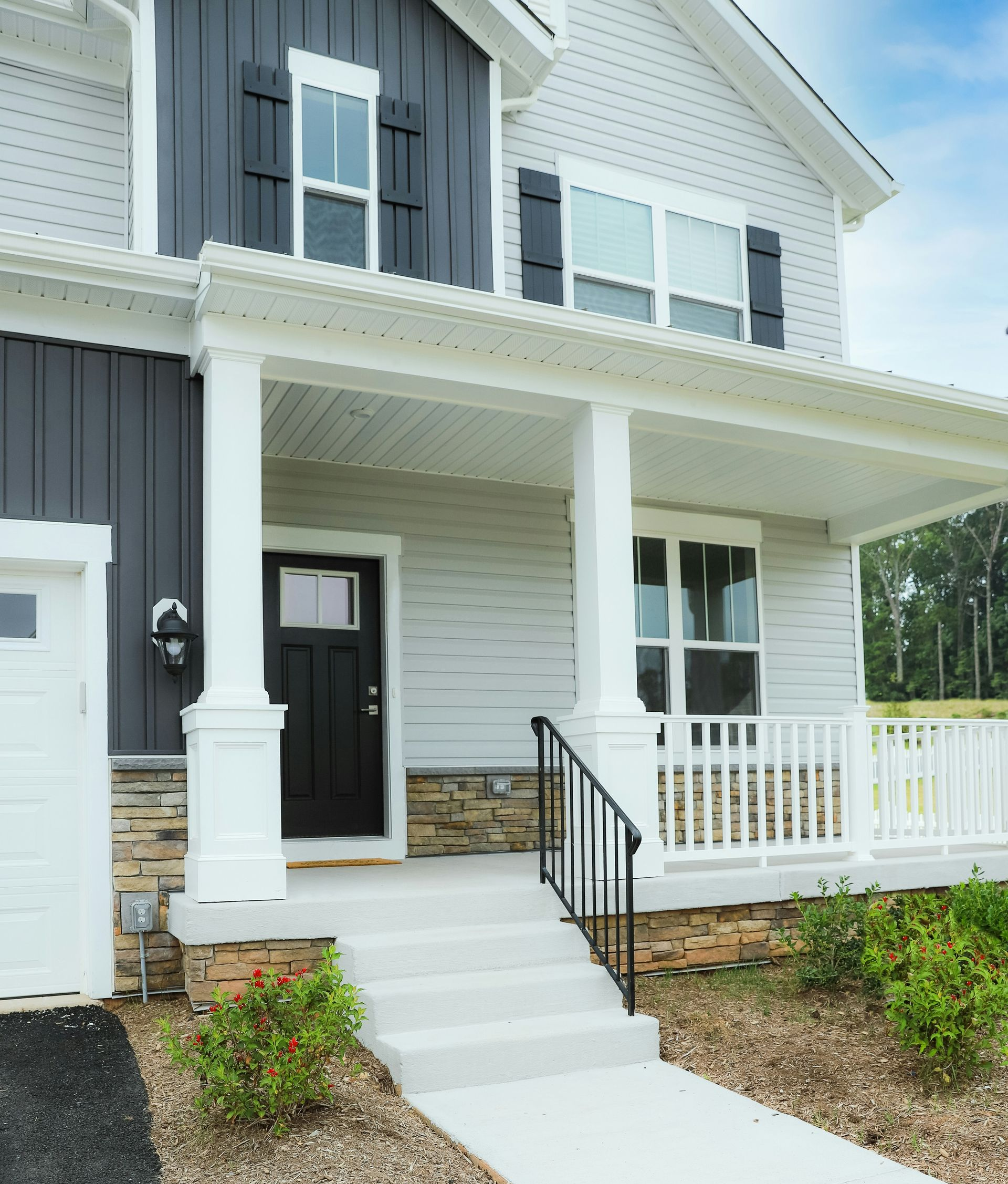 A two-story house exterior with light grey siding, dark board-and-batten accents, a stone foundation, and a front porch.