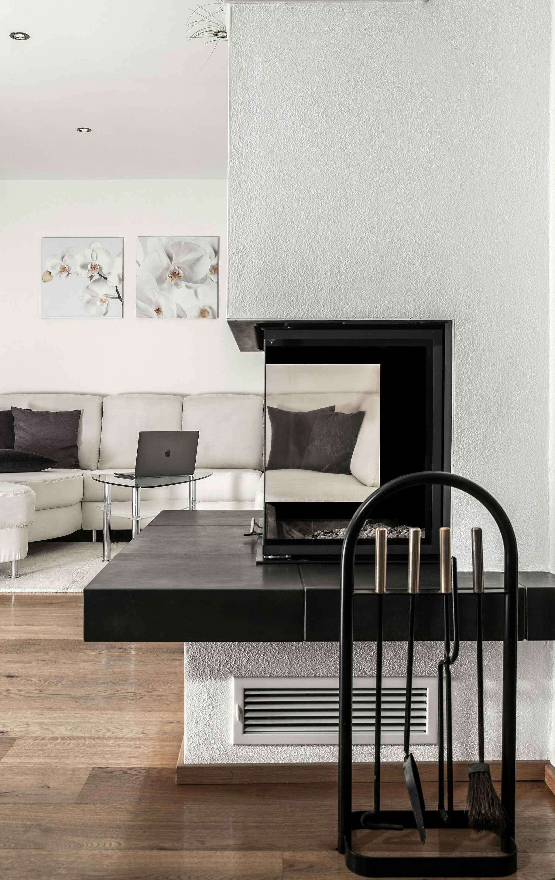 Modern living room with black fireplace, white walls, gray sofa, and black chair on wooden floor
