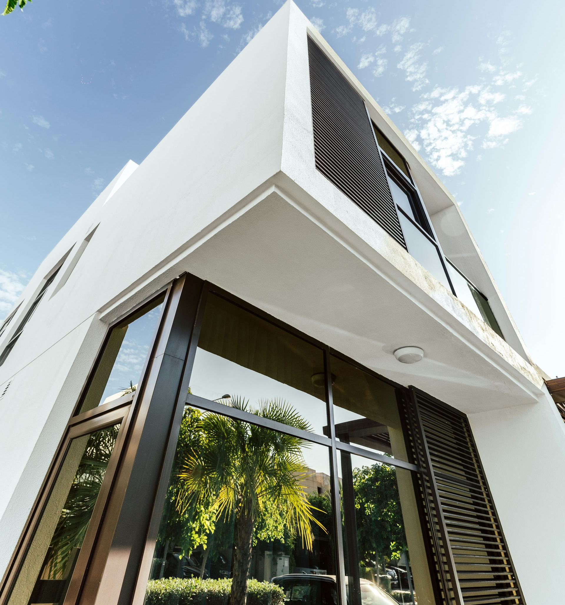 Modern white corner house with large glass windows and black louvered panels against a blue sky