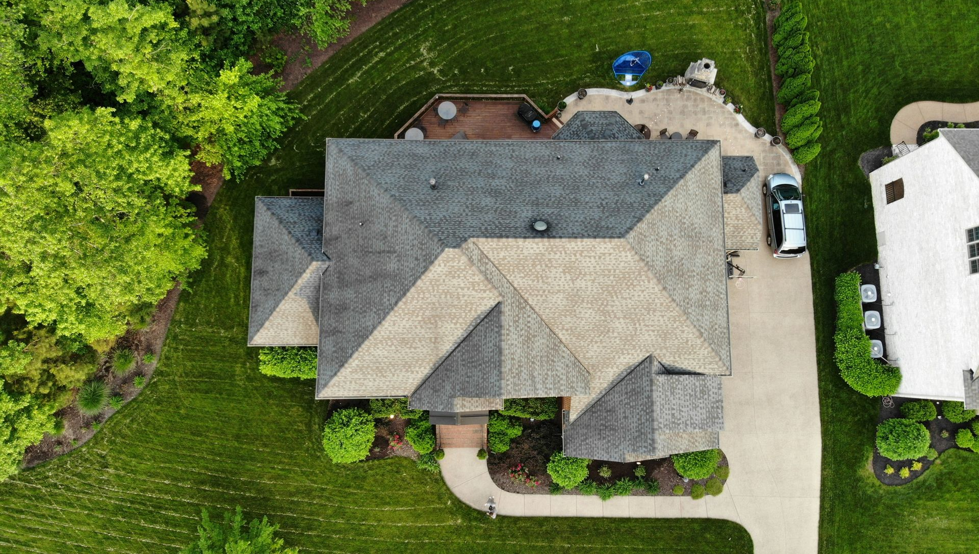Aerial view of a gray-roofed house with driveway, surrounded by green trees and lawn.