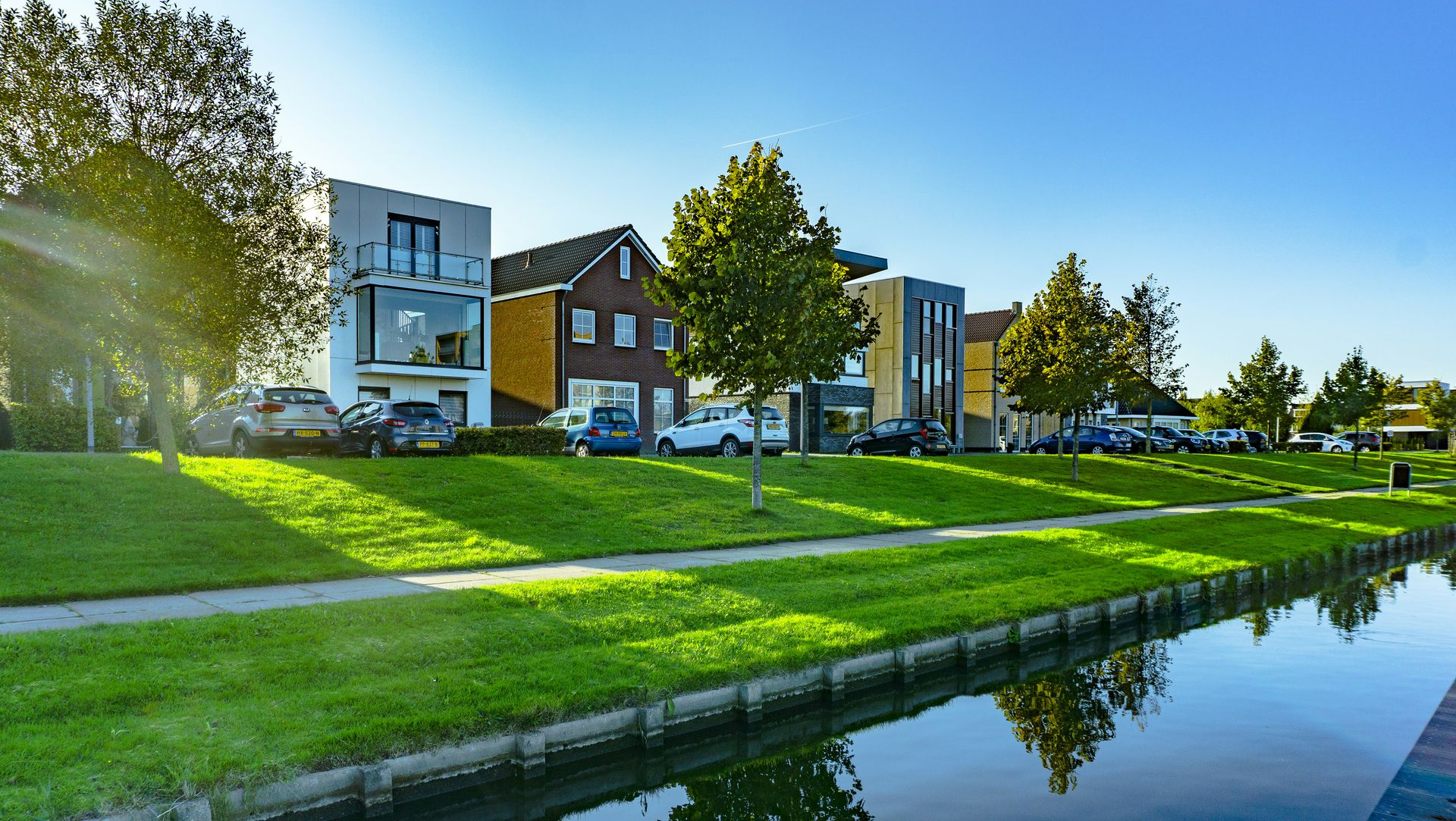 Modern apartment buildings beside a canal with green lawns and trees under a clear blue sky