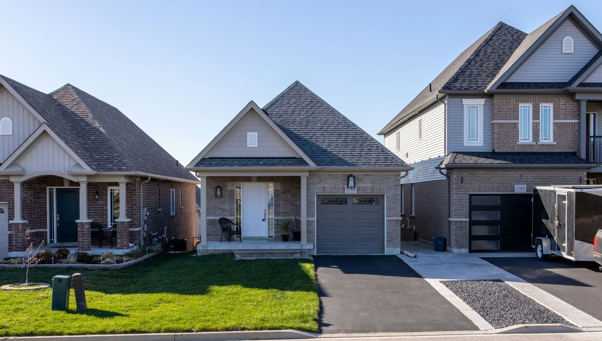 Row of modern suburban houses with driveways, garages, and neatly kept lawns under a clear sky