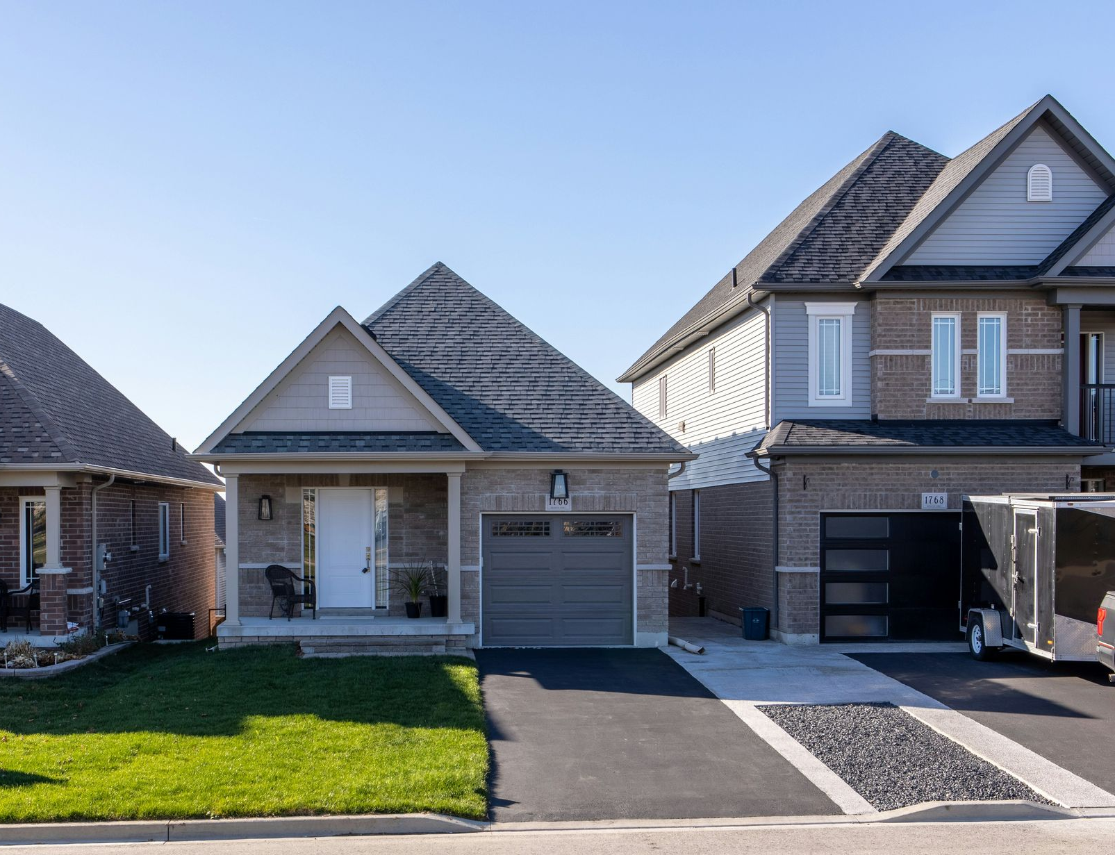 Row of suburban houses with garages, gray roofs, and a sunny front lawn