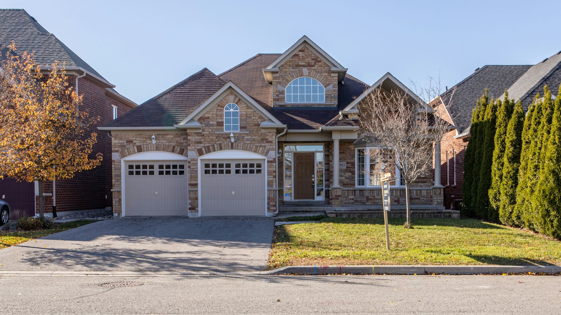 Suburban brick house with a two-car garage, arched windows, and a small front lawn.