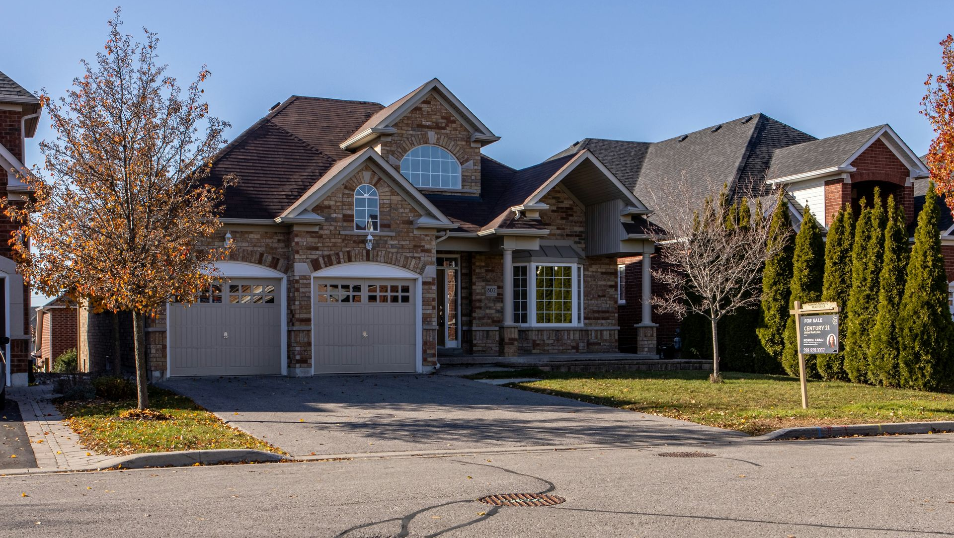 Suburban stone house with a two-car garage and autumn trees along a quiet street