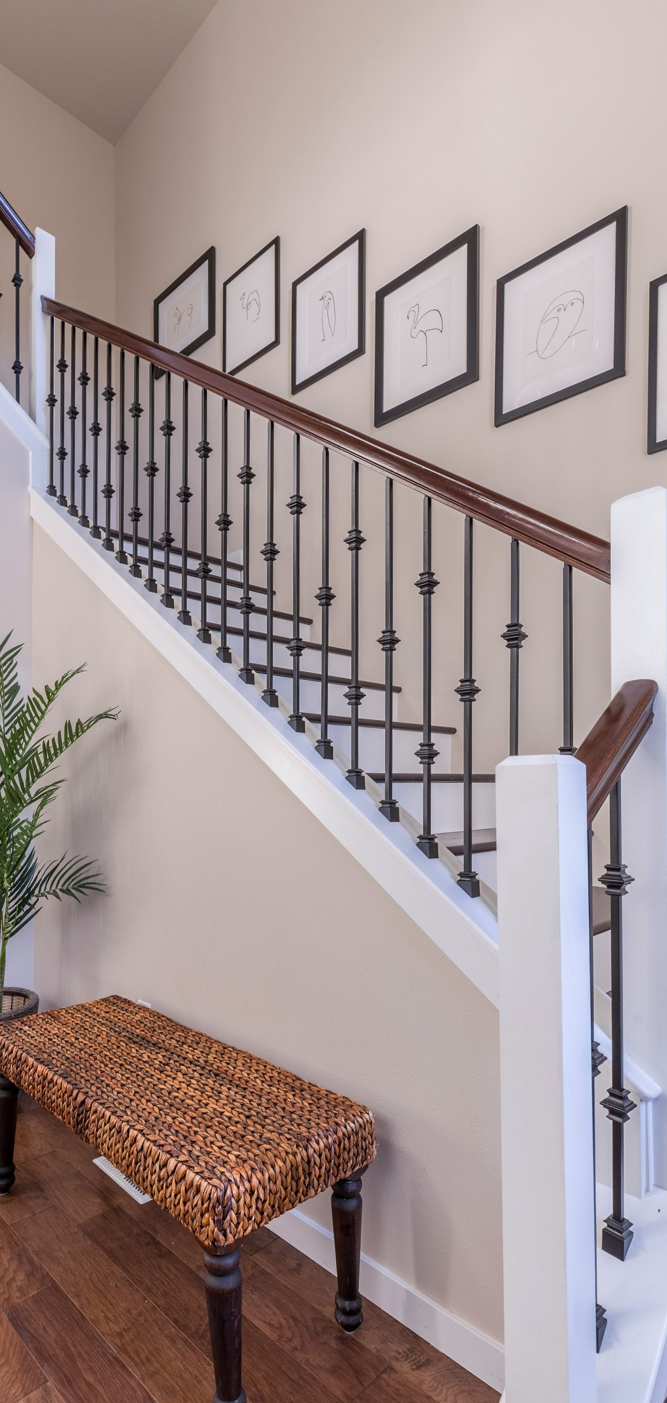Staircase with framed wall art, wooden bench, and potted plant in a bright entryway