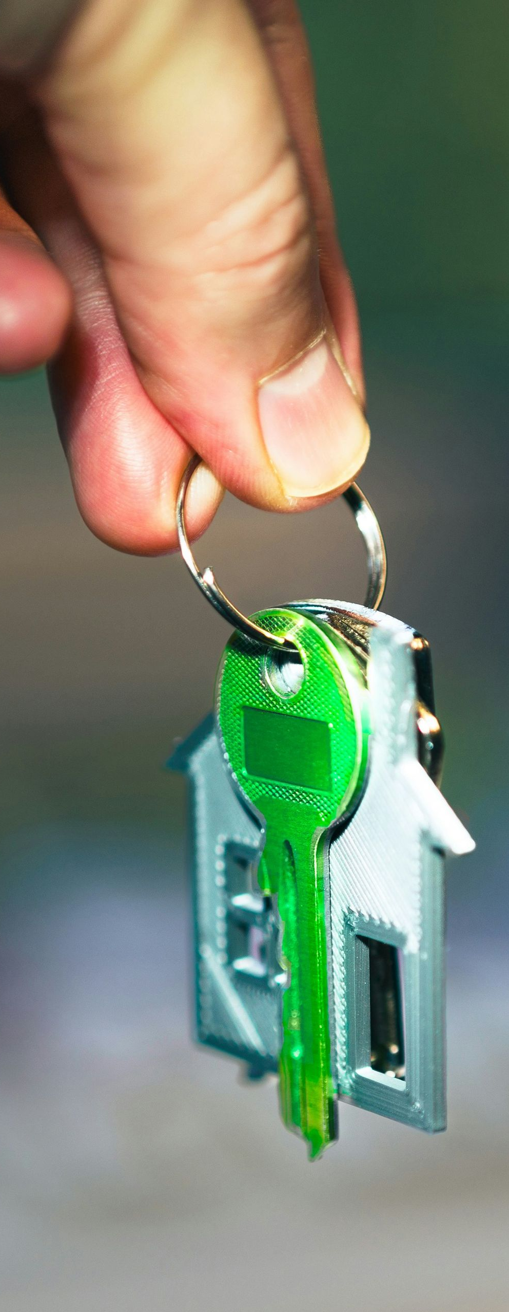Hand holding a key ring with a bright green key and metal house-shaped keychain