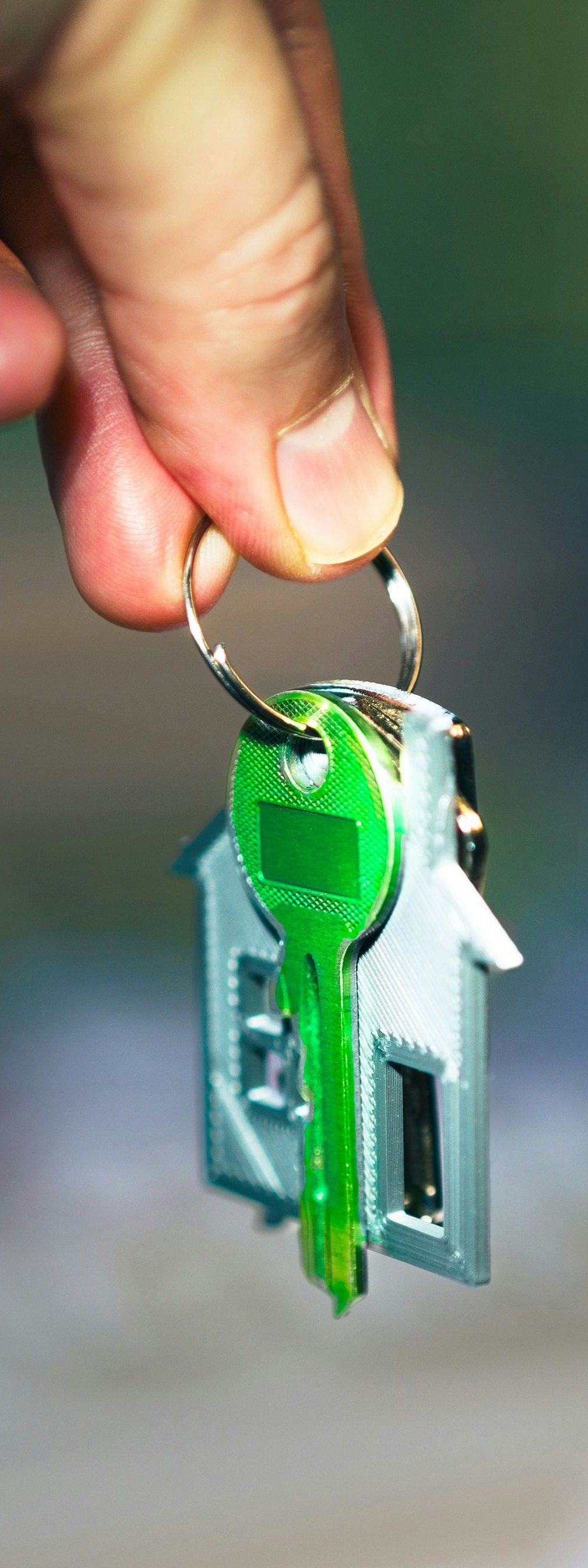 Hand holding a keyring with a green key and a house-shaped keychain