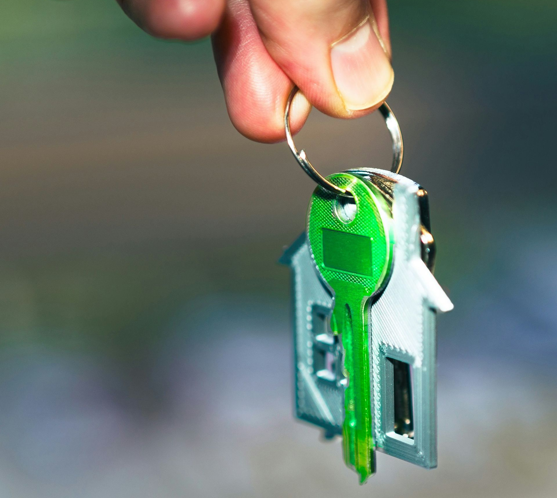 A hand holds a green key on a keyring shaped like a small house.