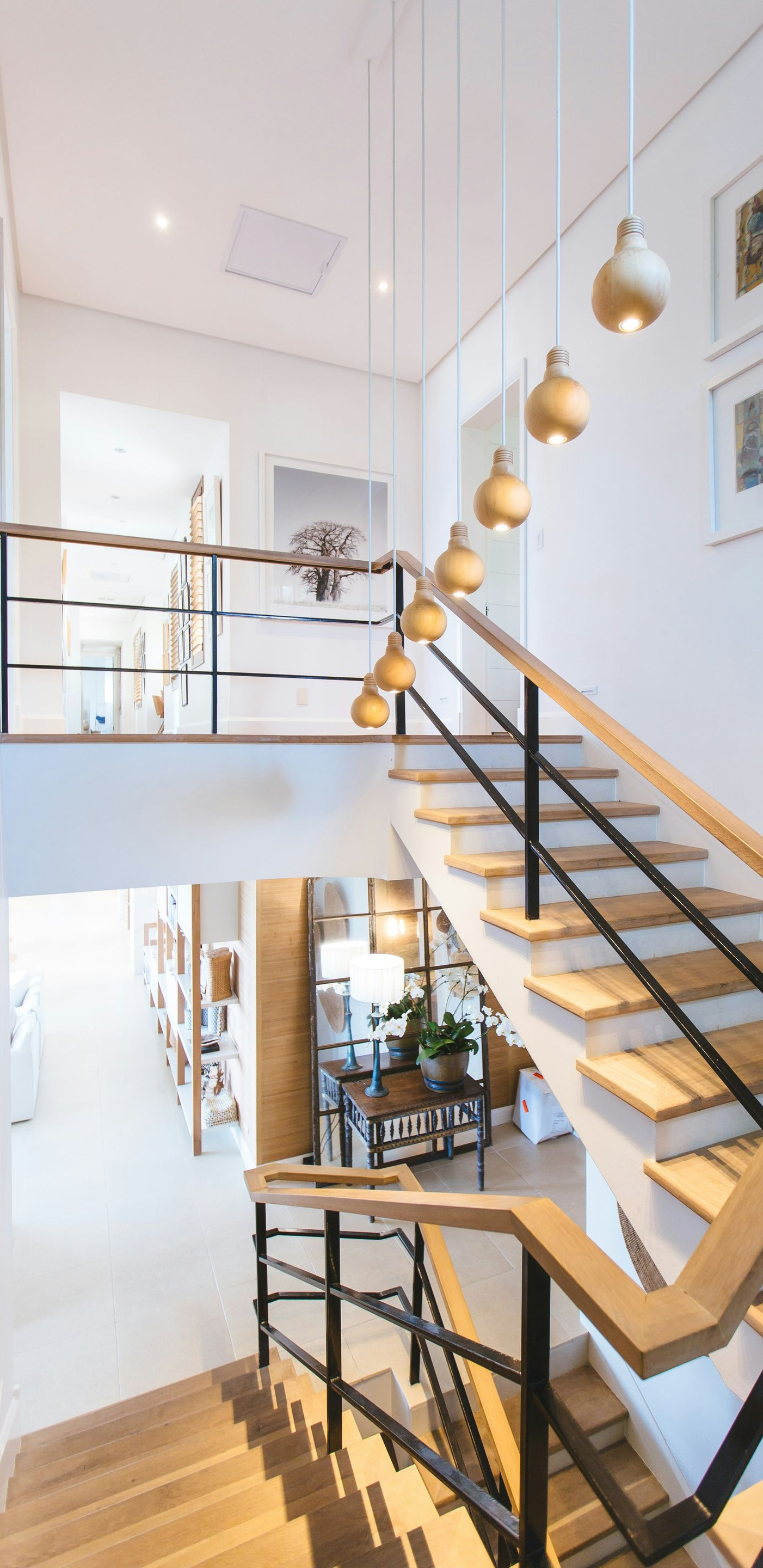 Modern stairwell with black railings, wood steps, and gold pendant lights in a bright white interior
