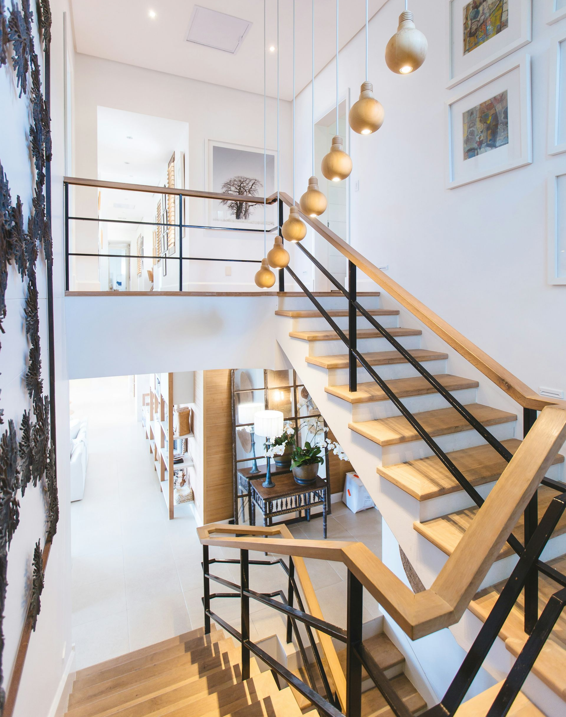 A modern staircase with wooden steps, black railings, and a series of pendant lights hanging above in a bright entryway.