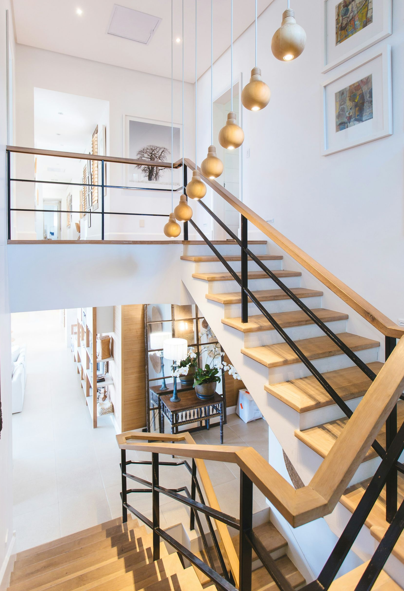A modern staircase with wooden steps, black railings, and a series of pendant lights hanging above in a bright entryway.