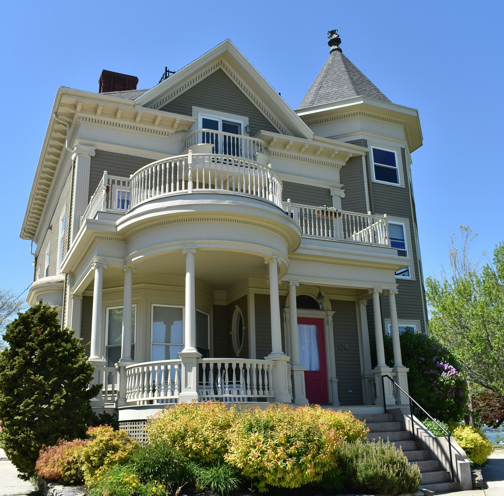 Two-story Victorian house with a turret, balcony, and porch, painted in green and cream, with a red front door.