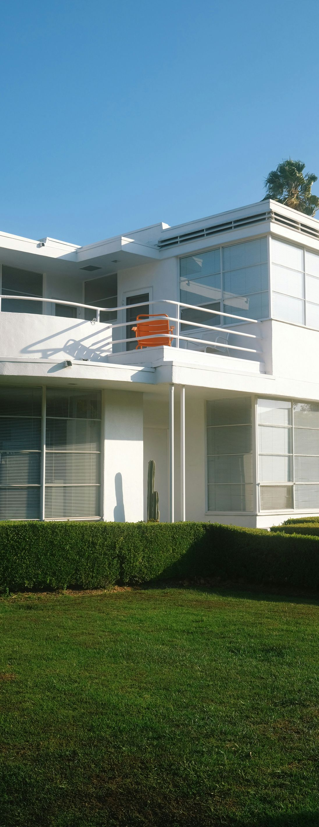 Modern white house with balconies, large windows, and a manicured green lawn under a clear blue sky