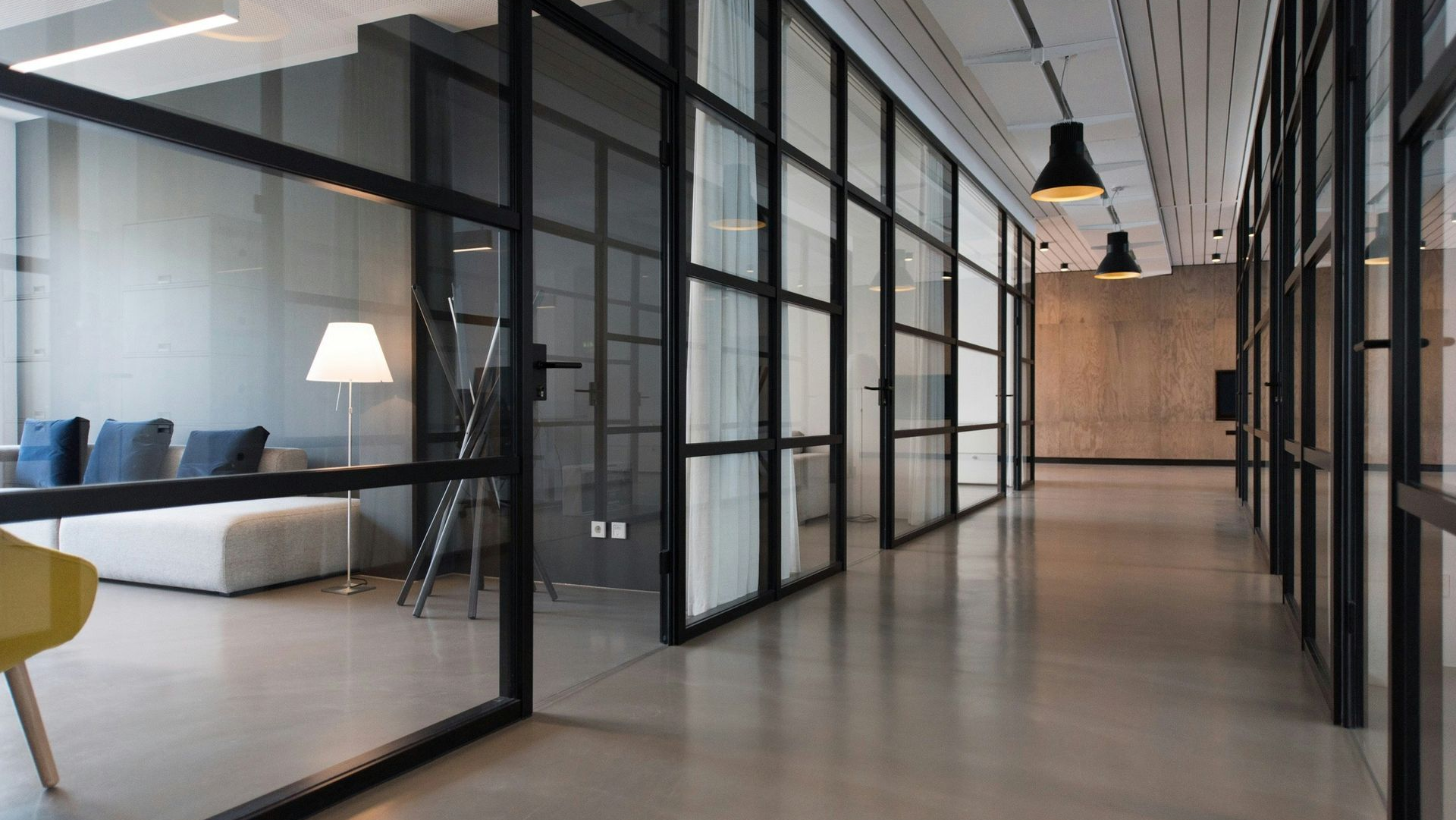 Modern office corridor with glass-walled meeting rooms, black frames, and a lounge area on the left