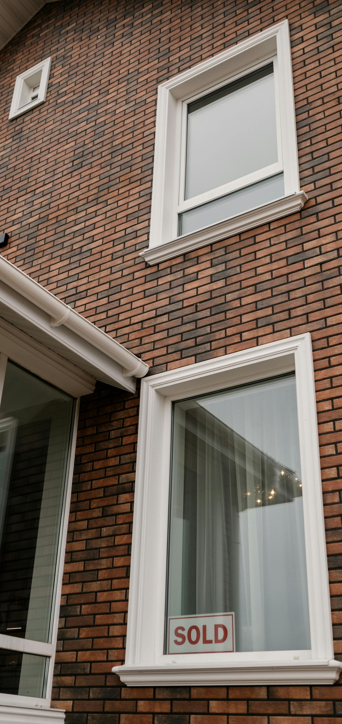 A brick house exterior with a white-framed window featuring a
