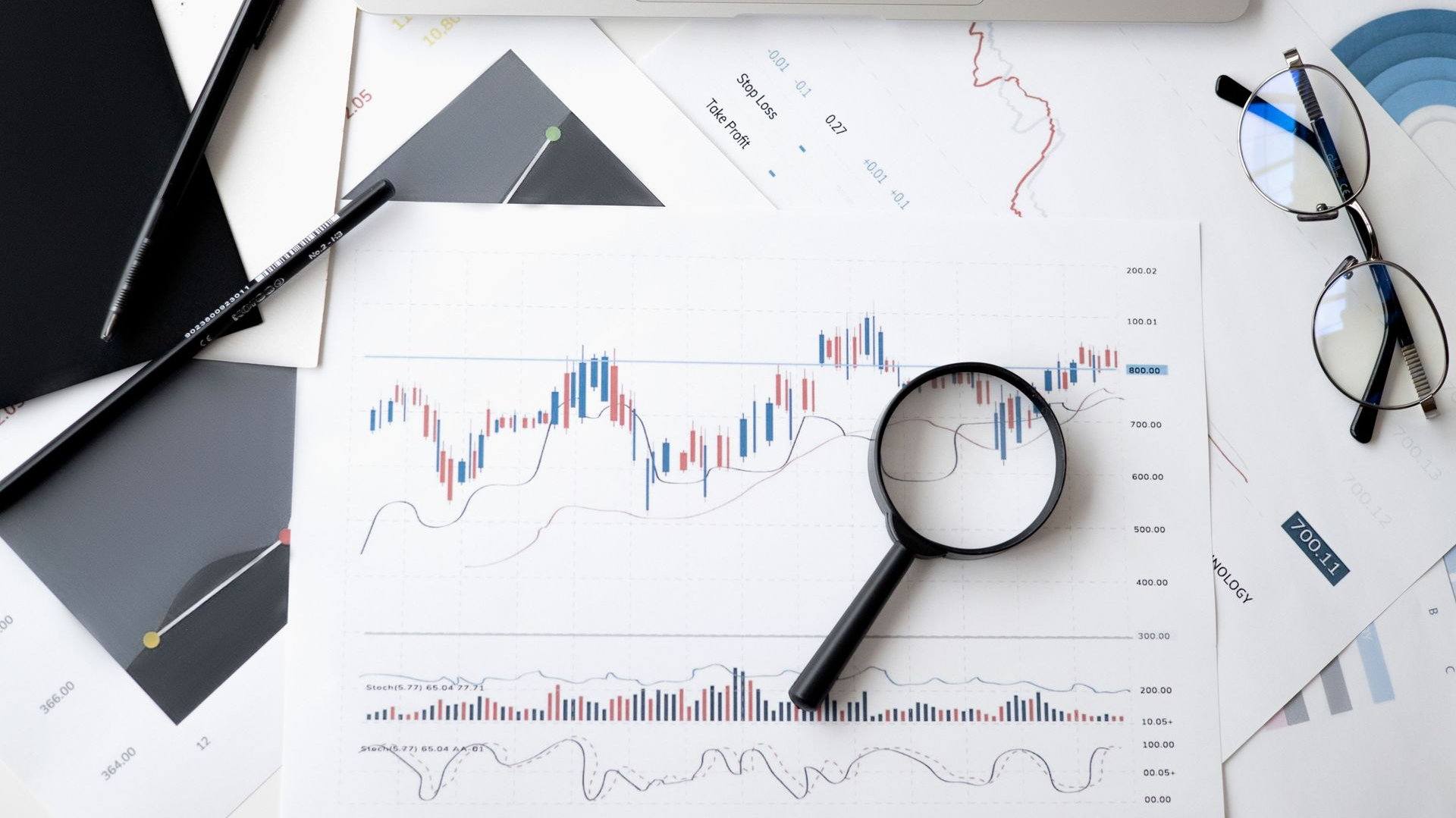 Business desk with charts, magnifying glass, glasses, and pen on white paper