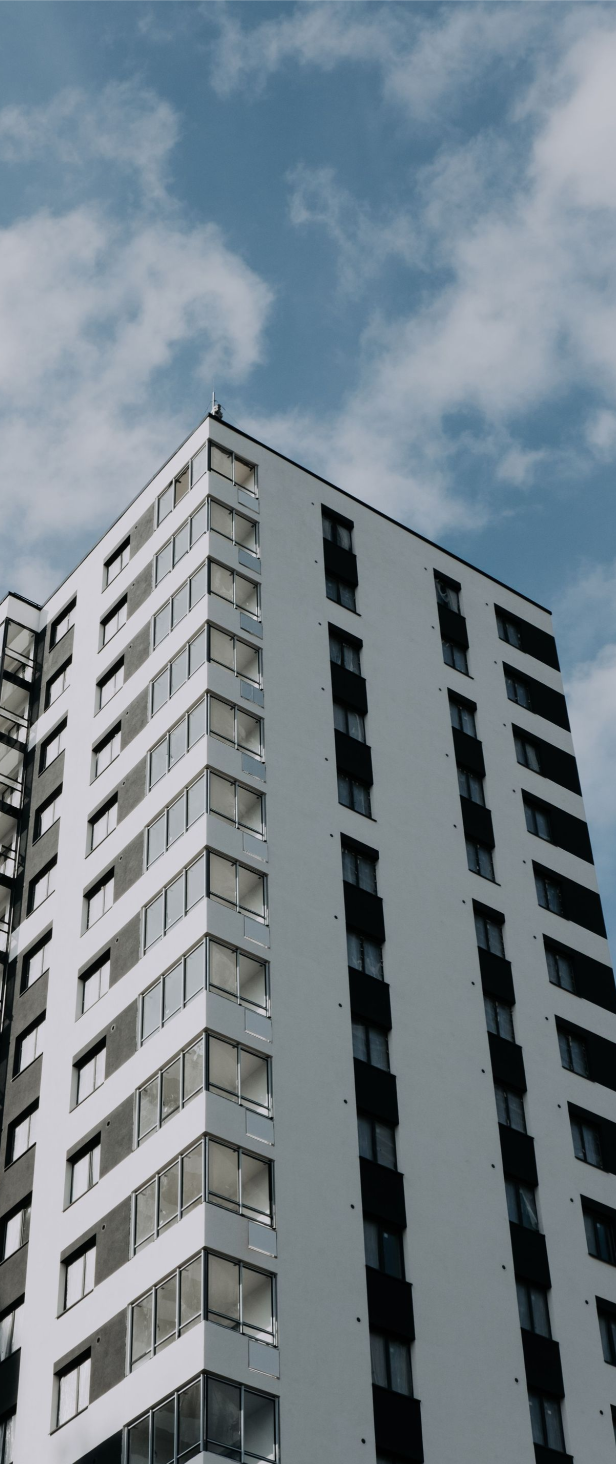 Low-angle view of a tall white apartment building against a cloudy blue sky