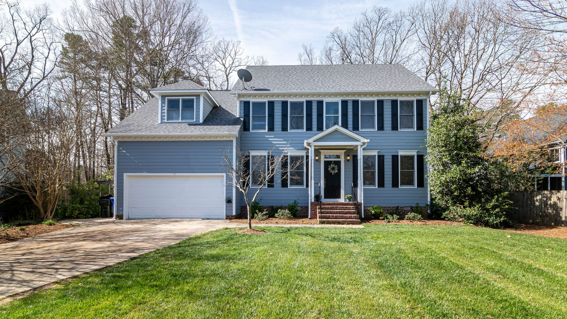 Two-story blue house with white trim, attached garage, and a large green front lawn.