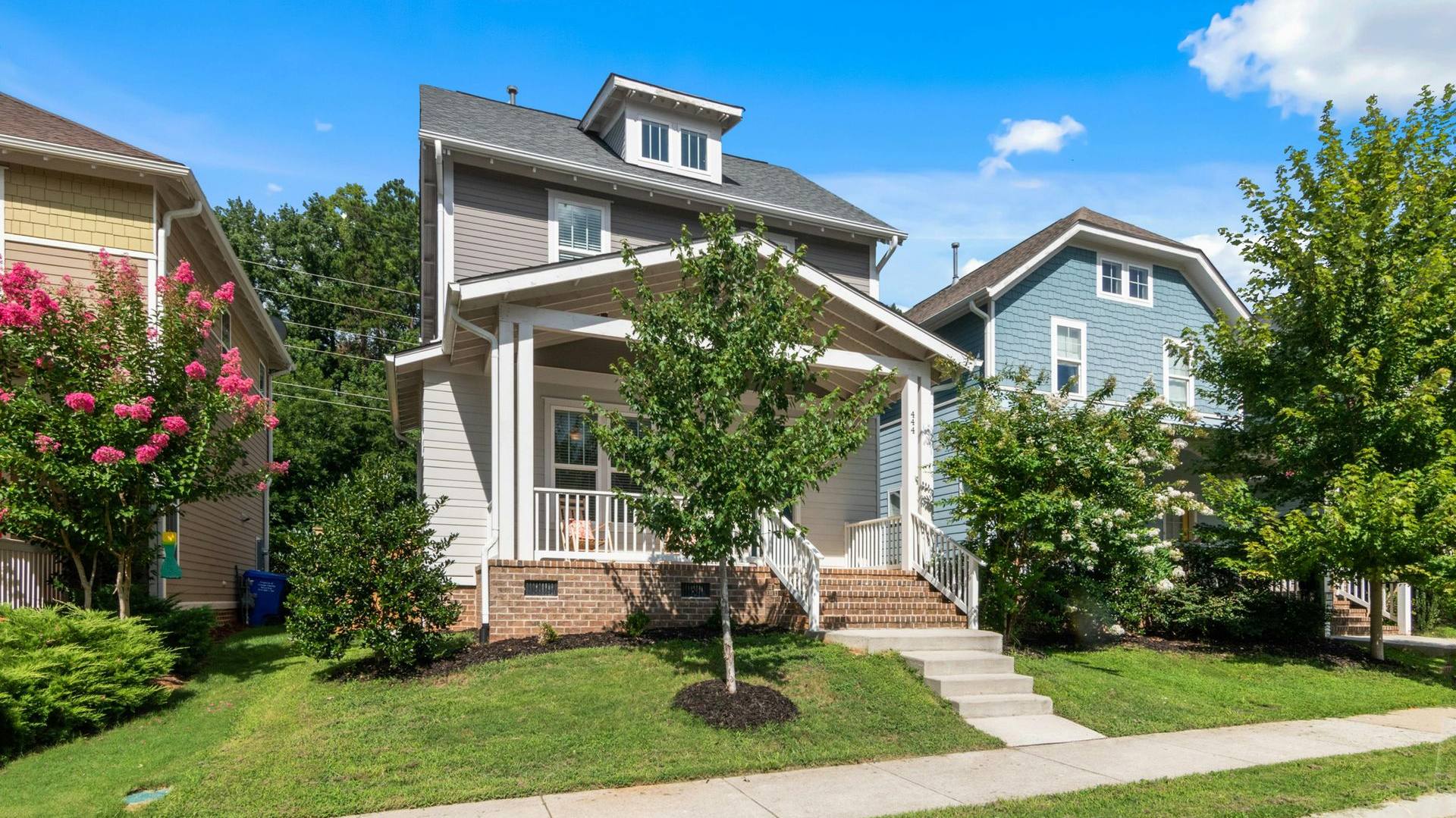 Suburban house with a front porch, white trim, and a manicured lawn on a sunny day